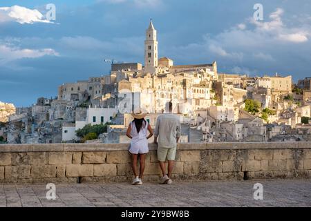 Una coppia si erge su un balcone in pietra, guardando lo skyline mozzafiato di Matera. Gli antichi edifici si crogiolano nel caldo bagliore del tramonto con la raccolta Foto Stock