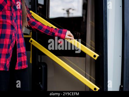 la ragazza scende dall'autobus alla fermata dell'autobus e rimane ferma al corrimano Foto Stock