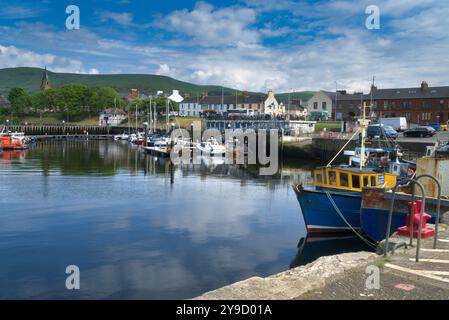 Guardando verso l'interno, verso ovest, dal molo di Girvan verso la città e il porto di Girvan. Barche da diporto lungo pontoni e grandi pescherecci ormeggiati nel porto. Gi Foto Stock