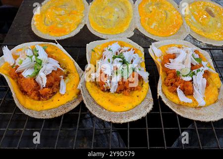 Gustosa varietà di frittelle croccanti tailandesi tradizionali o Khanom Bueang, con condimenti di cocco grattugiato e prezzemolo tritato in vendita Foto Stock