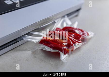 Sigillatrice sottovuoto con sacchetto di plastica di pepe rosso su un tavolo bianco, primo piano. Foto di alta qualità Foto Stock