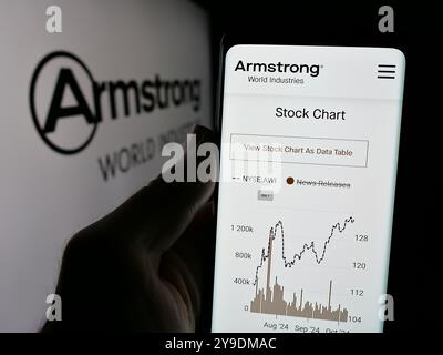 Persona che detiene lo smartphone con la pagina Web della società statunitense Armstrong World Industries Inc. Sullo schermo davanti al logo. Messa a fuoco al centro del display del telefono. Foto Stock