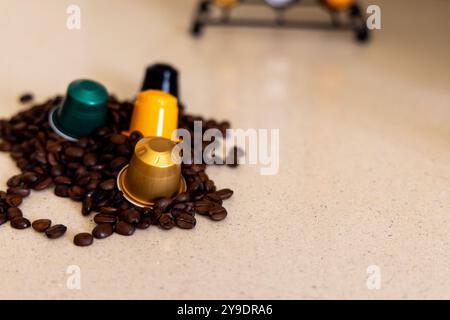 Le colorate capsule di caffè si trovano su un letto di chicchi di caffè tostati, con un elegante sistema anticapsule sullo sfondo. Una composizione dettagliata perfetta per il co Foto Stock