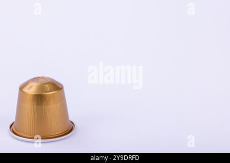 Una singola capsula di caffè dorata mostra eleganza su uno sfondo bianco luminoso Foto Stock