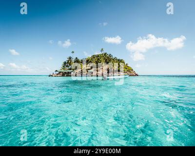 Una piccola isola circondata dalle acque oceaniche, caratterizzata da una barca che galleggia nelle vicinanze, creando una tranquilla scena costiera Foto Stock