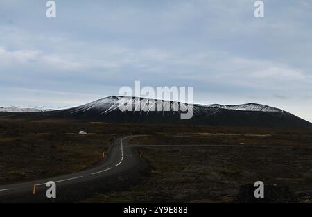 Collina vulcanica innevata con una strada tortuosa in primo piano, adagiata contro un cielo coperto e un paesaggio arido e aspro. Foto Stock