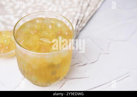 Gustoso tè a bolle in bicchiere e perle di tapioca sul tavolo bianco, primo piano. Spazio per il testo Foto Stock