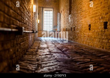 Lungo corridoio in mattoni di un antico edificio con finestra sullo sfondo corridoio di mattoni rossi delle prigioni del castello Estense di Ferrara Foto Stock