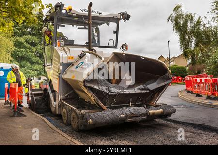 Un team di operai che gestiscono macchinari pesanti per ripavimentare una strada residenziale nel Wiltshire. Foto Stock