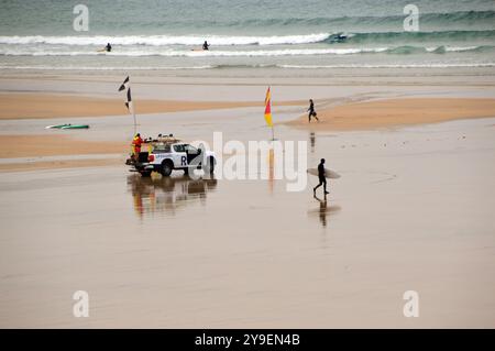 Surfer Walking con bagnini RNLI e veicolo Ford Ranger sulla spiaggia di Newquay Bay dal Southwest Coastal Path, North Cornwall, Inghilterra, Regno Unito. Foto Stock