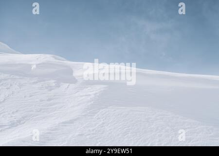 Una vasta e indisturbata distesa di neve si estende sotto un cielo limpido e blu. Creste delicate e ombre sottili creano un senso di pace e tranquillità. Foto Stock