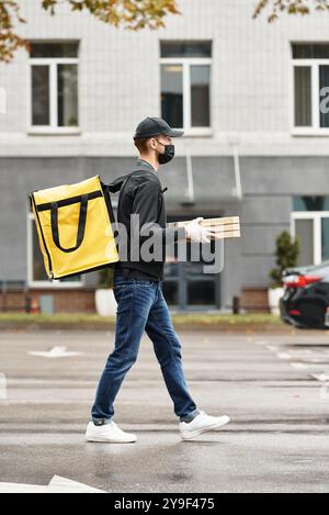 Un addetto alle consegne vestito di nero entra in un edificio per uffici mentre trasporta gli ordini di cibo durante il giorno. Foto Stock
