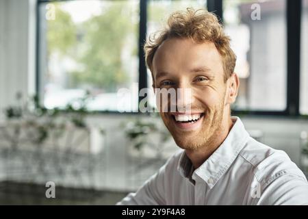 Un uomo d'affari impegnato con i capelli rossi sta lavorando diligentemente a un progetto in un ambiente d'ufficio contemporaneo. Foto Stock