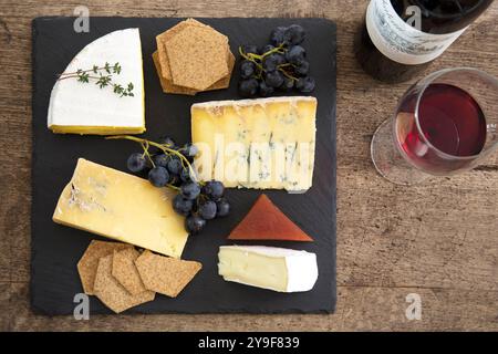 Un elegante tagliere di formaggi con selezioni artigianali, cracker e uva fresca abbinati perfettamente a un bicchiere di vino rosso per un lusso sofisticato Foto Stock