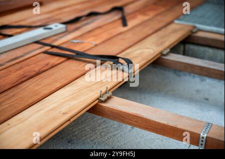 Un primo piano di pavimentazione in legno con dispositivi di fissaggio e attrezzi nascosti. Le tavole in legno sono fissate saldamente ai putrelli con viti, cinghie e b Foto Stock