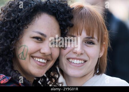 Ritratto ravvicinato di due giovani amiche che sorridono insieme. Donna dai capelli ricci con il simbolo della pace, vernice per il viso e testa rossa con l'anello del naso Foto Stock