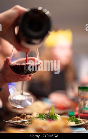 Un bicchiere di vino rosso che viene riempito da una bottiglia durante una cena di famiglia durante la stagione natalizia con vista ritratto. Foto Stock