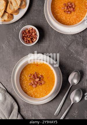 Fotografia gastronomica di zuppa di lenticchie rosse con peperoncino e pancetta, carote, cipolla, aglio, pane tostato, brodo, brodo, tabella Foto Stock