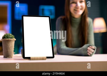 Concentrati su un tablet mockup presentato da Joyful Girl in background sfocato che fa un influencer marketing sponsorizzato dal brand. Primo piano di un dispositivo con schermo isolato sul tavolo pubblicizzato da star online Foto Stock