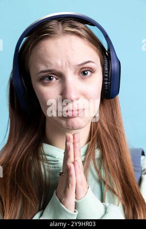 Donna che implorava il gesto della mano e si fa in posa, si trova in difficoltà, ha bisogno di favore, ha un background in studio. Primo piano di un adolescente che indossa le cuffie, gesti per favore, richiedendo assistenza Foto Stock