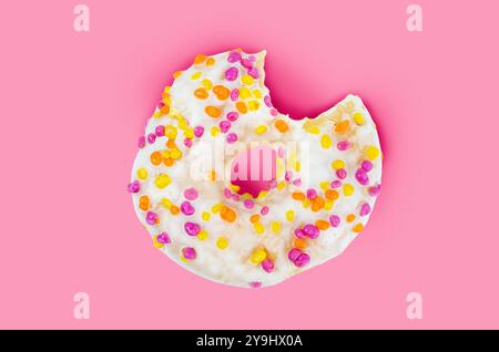 Manca un boccone di ciambella al cioccolato bianco con macchie multicolori su sfondo rosa. Foto Stock