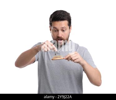 Uomo emotivo che prende i capelli persi da una spazzola su sfondo bianco. Problema di alopecia Foto Stock