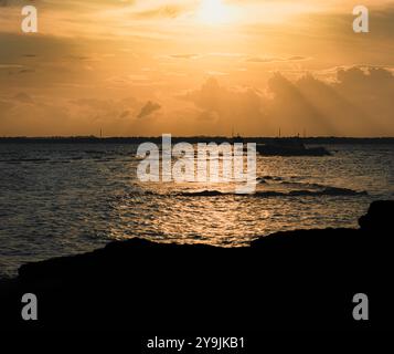 La luce del sole crea i raggi del sole, proiettando un caldo bagliore sulla scena tranquilla. Le barche sagomate si piegano dolcemente in lontananza, mentre le acque calme si riflettono Foto Stock