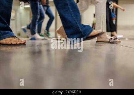 Diverse coppie di gambe e piedi si muovono su un pavimento lucido in quello che sembra essere un luogo pubblico. L'attenzione è sulle gambe e sulle scarpe, con un po' Foto Stock