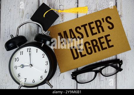 Testo di laurea magistrale su carta con sveglia vista dall'alto su sfondo in legno Foto Stock