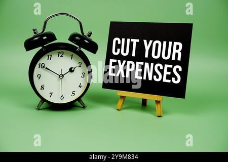 Riduci i messaggi di testo sulle spese su carta con il clcok di allarme su sfondo in legno Foto Stock