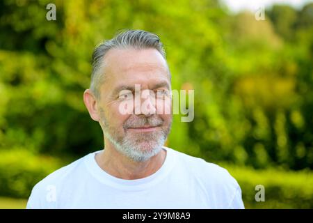 Un uomo maturo con capelli grigi e una barba ben rifinita, indossa una T-shirt bianca Foto Stock