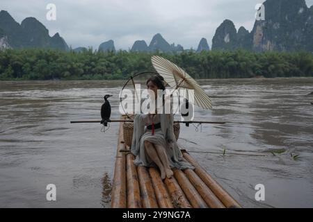 Hanfu ragazza con ombrello su zattera di bambù in Xingping in posa con cormorani Foto Stock