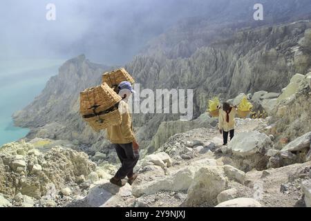 I minatori di zolfo si arrampicano sulle pareti della caldera del cratere Ijen con un carico medio di 90 kg. Foto Stock