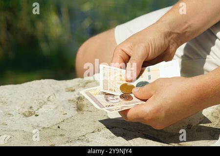 Le mani di un uomo che tiene la moneta nazionale della Bosnia-Erzegovina. La persona detiene 210 marchi bosniaci convertibili in banconote e diverse monete Foto Stock