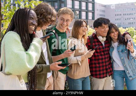 Un gruppo di giovani studenti che sorridono e utilizzano smartphone insieme in un campus universitario. L'immagine cattura l'amicizia, l'uso della tecnologia e l'inclusività Foto Stock