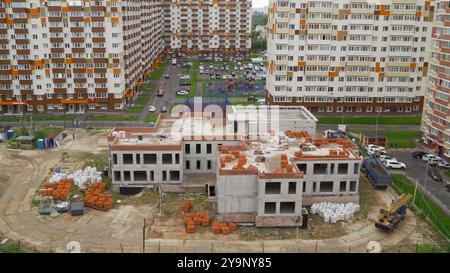 Cantiere di un asilo nido in una nuova area residenziale con una gru che consegna mattoni Foto Stock