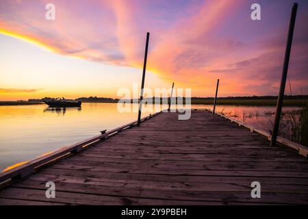 Una vecchia banchina di legno e una barca su un tranquillo lago riflettente al tramonto Foto Stock