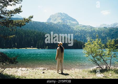 La donna sta accanto all'acqua sullo sfondo di foresta e montagna Foto Stock