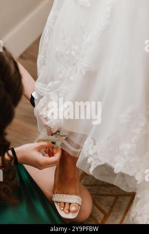 Damigella d'onore che chiude la scarpa impreziosita da perle della sposa Foto Stock