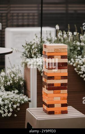 Grande torre di legno Jenga su un tavolo all'aperto, circondata da fiori Foto Stock