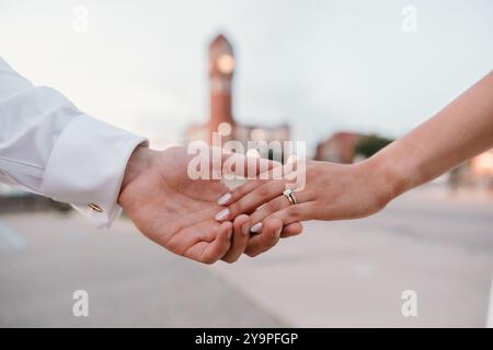 Sposa e sposo che tengono le mani, torre dell'orologio sfocata sullo sfondo Foto Stock