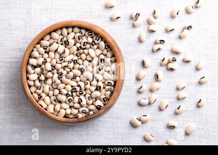 Piselli secchi con gli occhi neri in un recipiente di legno sopra il lino. Fagioli dagli occhi neri, o blackeye californiano, un legume di fagioli pallidi di medie dimensioni, con macchie nere. Foto Stock