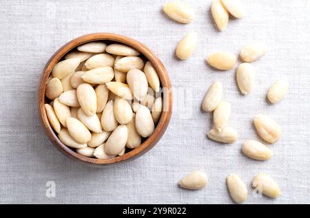 Mandorle appena sfornate in una ciotola di legno su lino. Mandorle sgusciate che sono state trattate con acqua calda per ammorbidire il rivestimento di semi, che viene quindi rimosso. Foto Stock