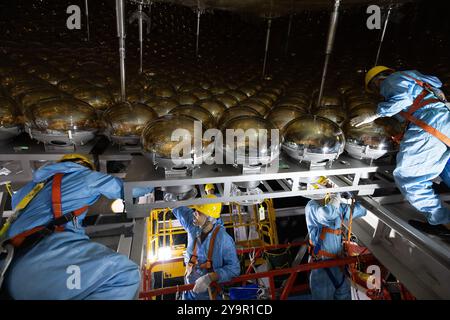 (241011) -- JIANGMEN, 11 ottobre 2024 (Xinhua) -- i membri del personale installano tubi fotomoltiplicatori del rivelatore centrale dell'Osservatorio neutrino sotterraneo di Jiangmen (JUNO) a Jiangmen, nella provincia del Guangdong della Cina meridionale, 9 ottobre 2024. La Cina ha costruito il rivelatore sferico trasparente più grande del mondo a 700 metri sottoterra per catturare neutrini sfuggenti, spesso soprannominati "particelle fantasma", per svelare i segreti di infinitesimamente piccoli e infinitamente vasti dell'universo. La sfera acrilica alta 12 piani con un diametro di 35,4 metri, sepolta in profondità in uno strato di granito di una collina in kaip Foto Stock