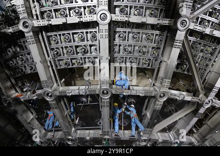 (241011) -- JIANGMEN, 11 ottobre 2024 (Xinhua) -- i membri del personale lavorano su una struttura in acciaio inossidabile del rivelatore centrale del Jiangmen Underground Neutrino Observatory (JUNO) a Jiangmen, nella provincia del Guangdong della Cina meridionale, 10 ottobre 2024. La Cina ha costruito il rivelatore sferico trasparente più grande del mondo a 700 metri sottoterra per catturare neutrini sfuggenti, spesso soprannominati "particelle fantasma", per svelare i segreti di infinitesimamente piccoli e infinitamente vasti dell'universo. La sfera acrilica alta 12 piani con un diametro di 35,4 metri, sepolta in profondità in uno strato di granito di una collina a Ka Foto Stock