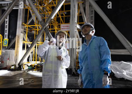 (241011) -- JIANGMEN, 11 ottobre 2024 (Xinhua) -- ma Xiaoyan (L) parla con un membro del personale sul fondo del serbatoio d'acqua del rivelatore centrale dell'Osservatorio neutrino sotterraneo di Jiangmen (JUNO) a Jiangmen, nella provincia del Guangdong della Cina meridionale, 10 ottobre 2024. La Cina ha costruito il rivelatore sferico trasparente più grande del mondo a 700 metri sottoterra per catturare neutrini sfuggenti, spesso soprannominati "particelle fantasma", per svelare i segreti di infinitesimamente piccoli e infinitamente vasti dell'universo. Sfera acrilica alta 12 piani con un diametro di 35,4 metri, sepolta in profondità in un gr Foto Stock