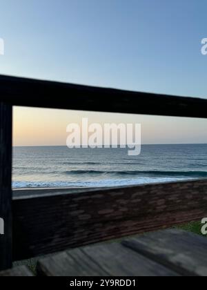 Tramonto sull'Oceano Atlantico visto attraverso una ringhiera di legno sul lungomare di Ribeira grande, sull'isola di São Miguel, Azzorre. Foto Stock