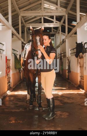 Giovane donna in uniforme equestre in stalla accanto al suo cavallo Foto Stock