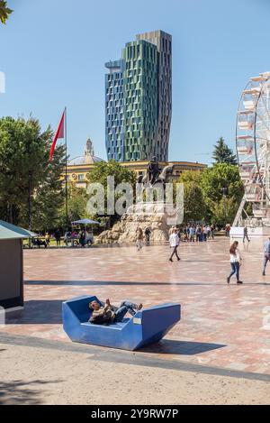 Un uomo giace su una panchina a leggere in piazza Skanderberg a Tirana Foto Stock