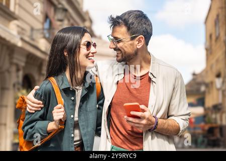 I giovani turisti hipster alternativi sono una coppia innamorata di passeggiare all'aperto lungo la strada della città, abbracciandosi e indossando un guardaroba moderno e alla moda. Fashi Foto Stock